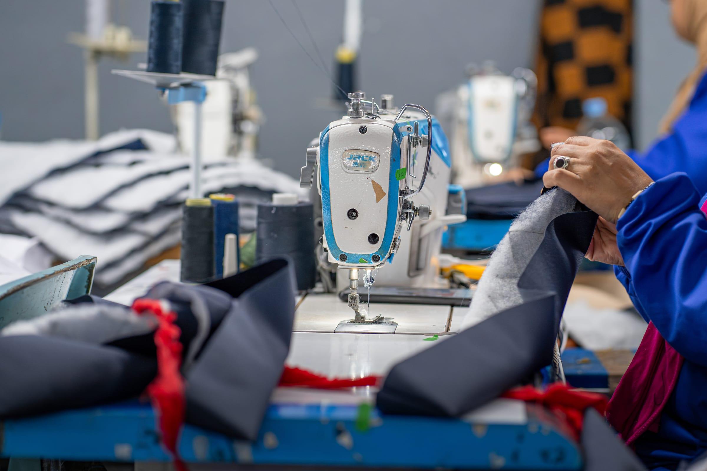 A machinist's hands guiding navy fabric under the head of an industrial sewing machine