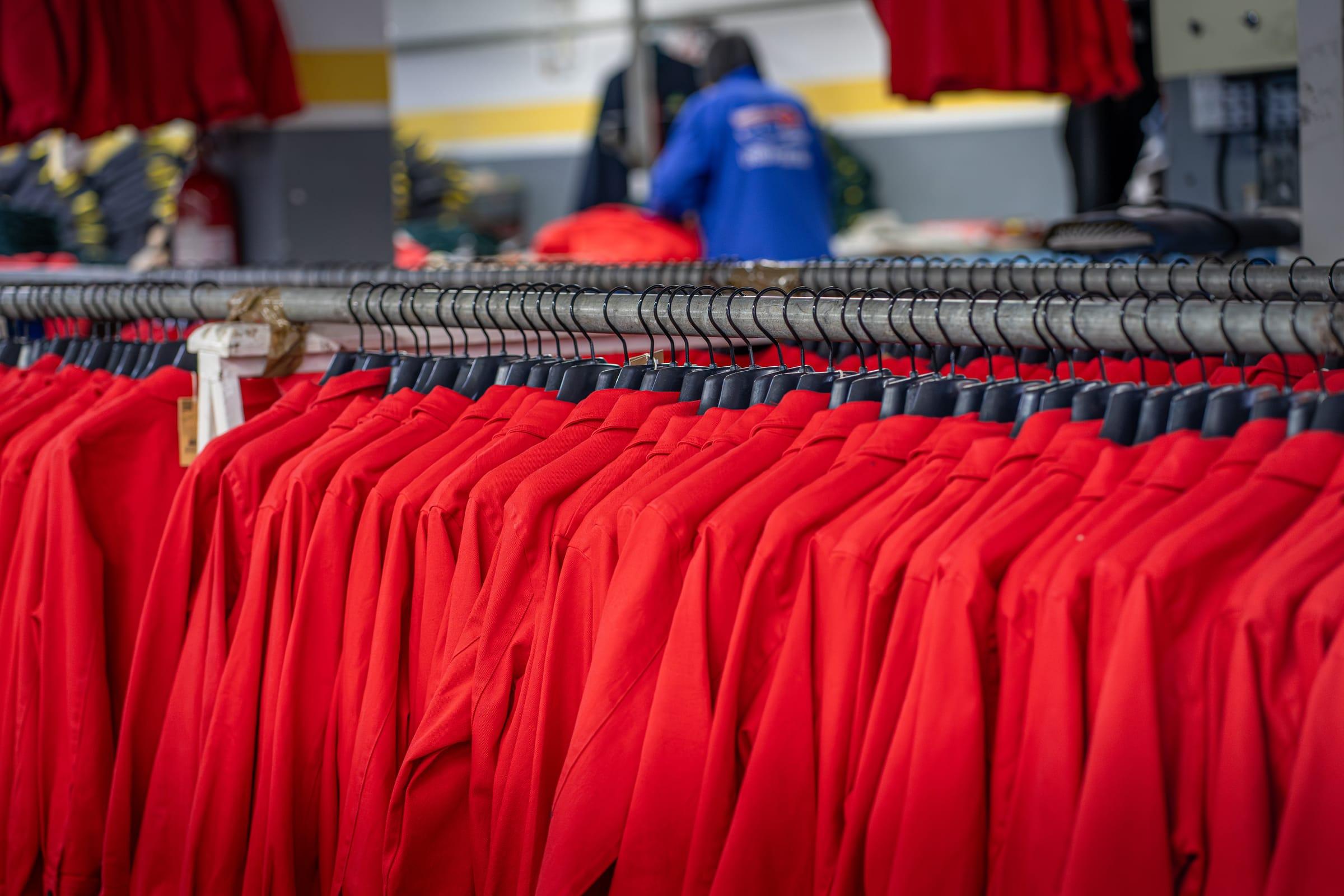 Portant de vestes de travail rouges identiques, alignées sur cintres dans l'atelier PROVETEX avant expédition