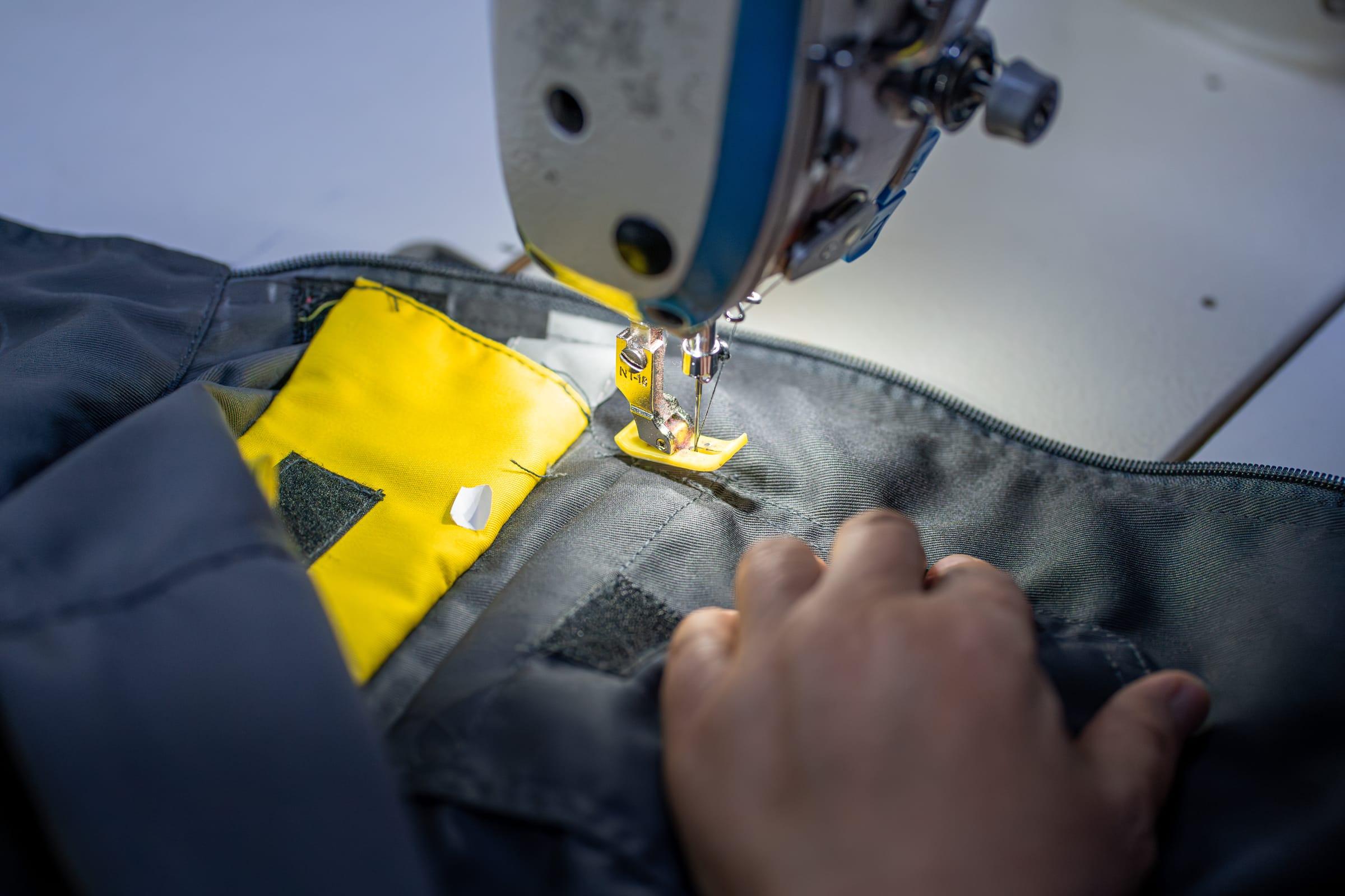 Couture d'un empiècement jaune haute visibilité sur une veste de travail grise, sous l'aiguille d'une machine industrielle