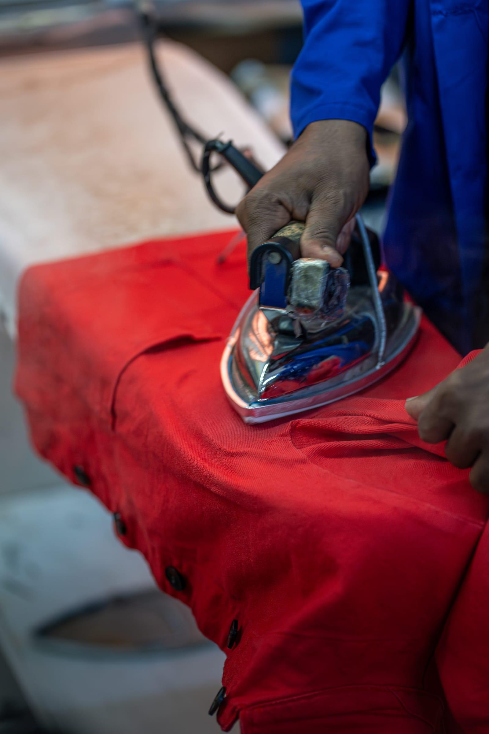 Repassage au fer à vapeur d'une veste de travail rouge sur la table de finition