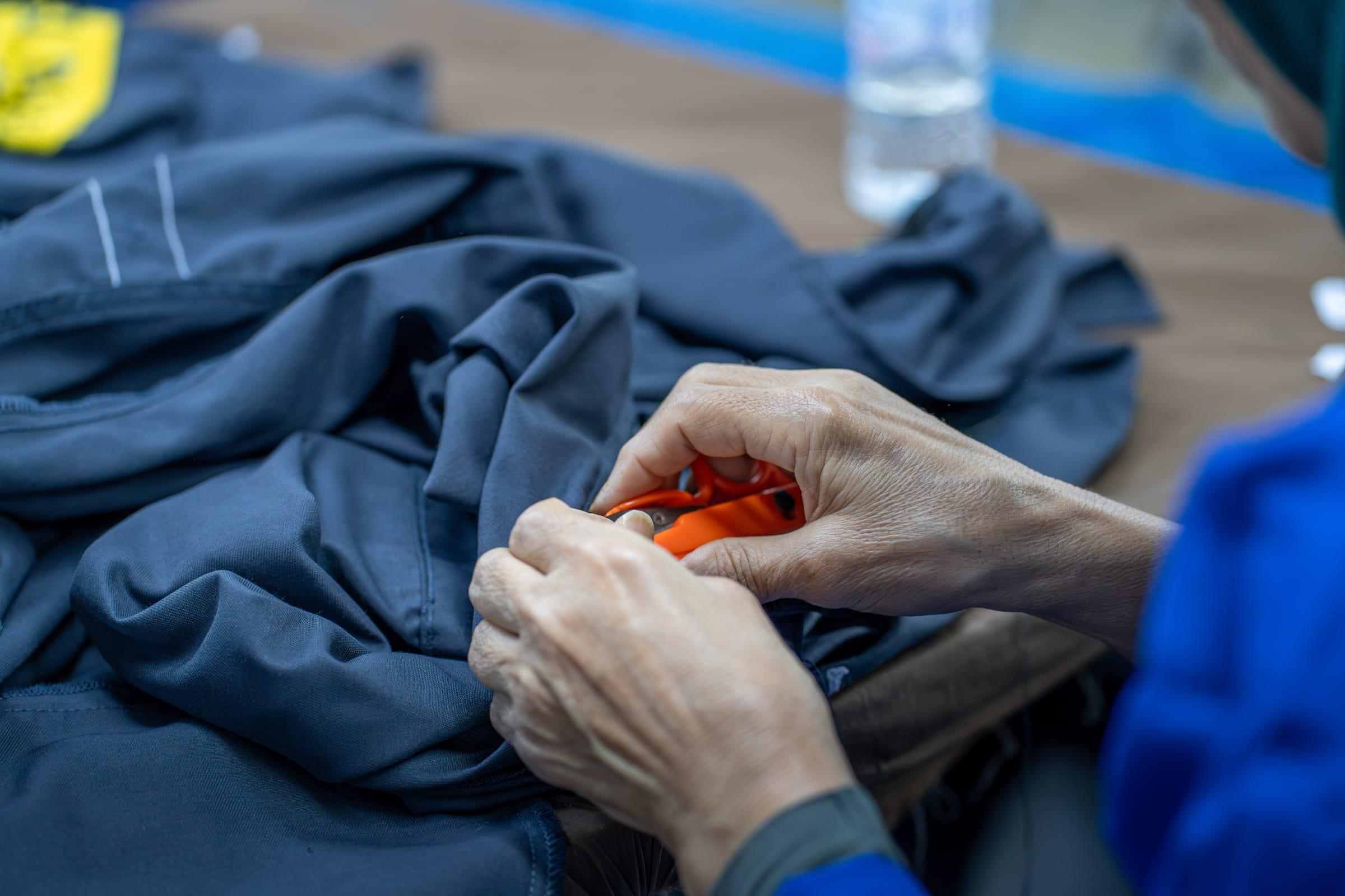 Mains coupant les fils d'une veste de travail bleu marine lors du contrôle finition dans l'atelier PROVETEX